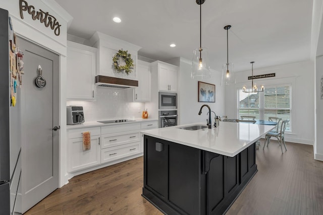 kitchen featuring built in microwave, sink, pendant lighting, a center island with sink, and white cabinets