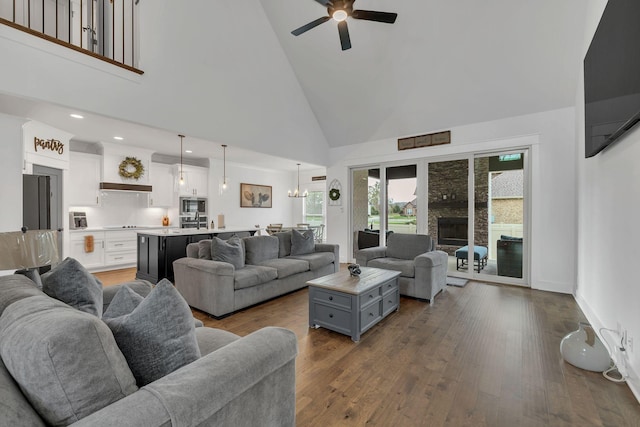 living room featuring high vaulted ceiling, ceiling fan with notable chandelier, sink, a fireplace, and wood-type flooring