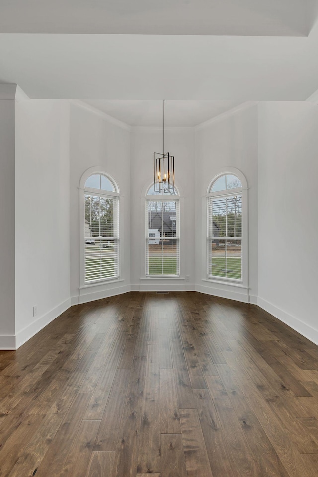 unfurnished dining area featuring crown molding, dark wood-type flooring, and an inviting chandelier