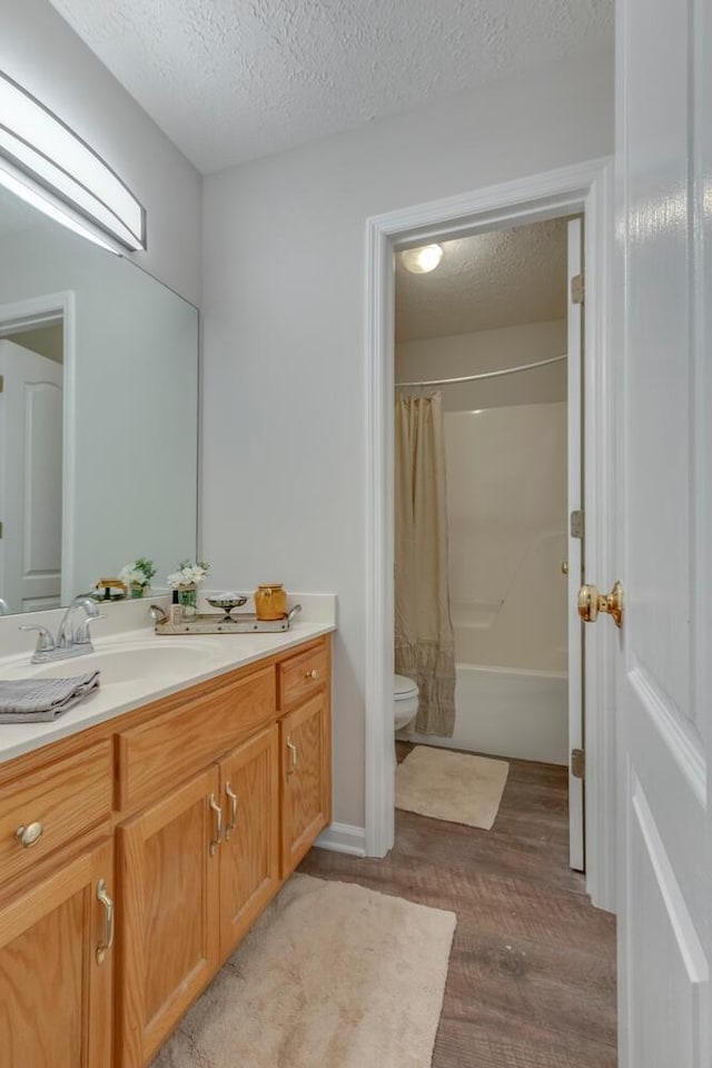 full bathroom with a textured ceiling, vanity, wood-type flooring, shower / bathtub combination with curtain, and toilet