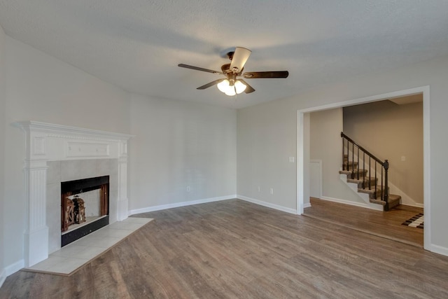 unfurnished living room featuring ceiling fan, light wood-type flooring, a textured ceiling, and a tile fireplace