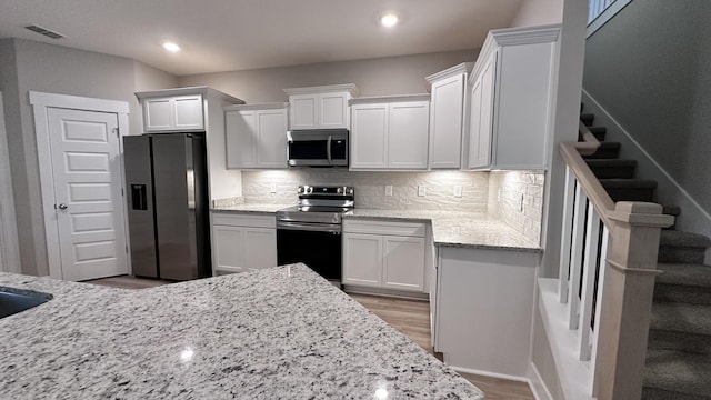 kitchen with white cabinets, light hardwood / wood-style flooring, decorative backsplash, appliances with stainless steel finishes, and light stone counters