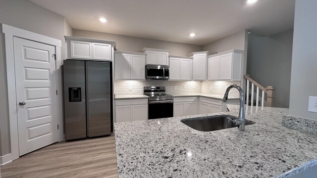 kitchen featuring kitchen peninsula, sink, decorative backsplash, appliances with stainless steel finishes, and white cabinetry