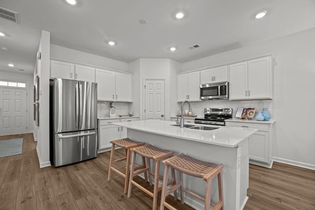 kitchen with backsplash, a kitchen island with sink, white cabinets, sink, and stainless steel appliances