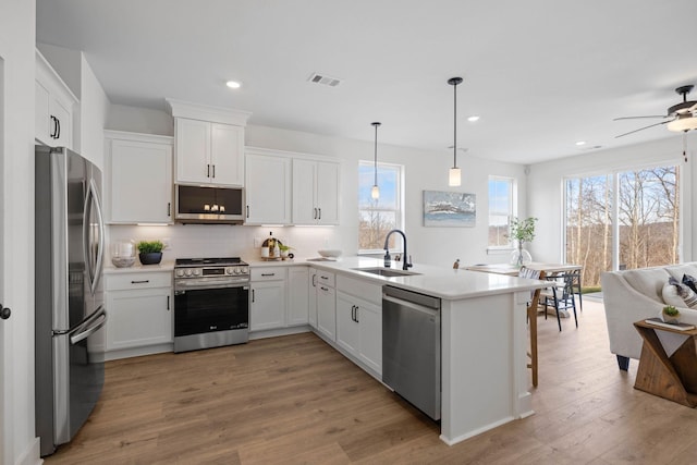 kitchen with appliances with stainless steel finishes, sink, wood-type flooring, pendant lighting, and white cabinetry