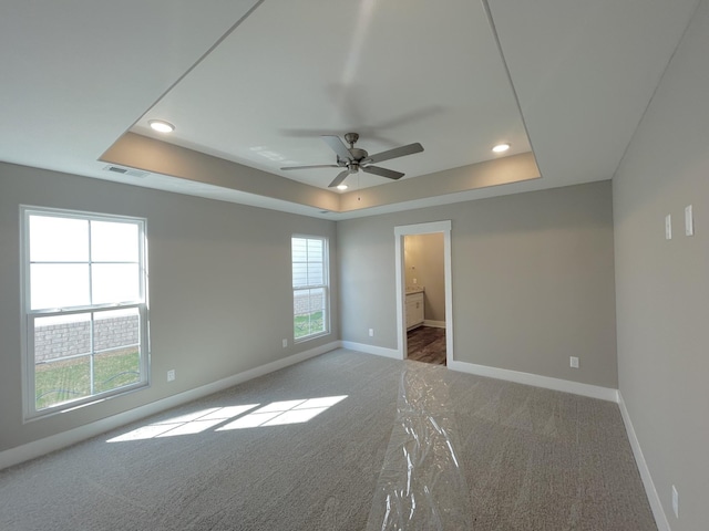 carpeted spare room featuring a tray ceiling, ceiling fan, and plenty of natural light