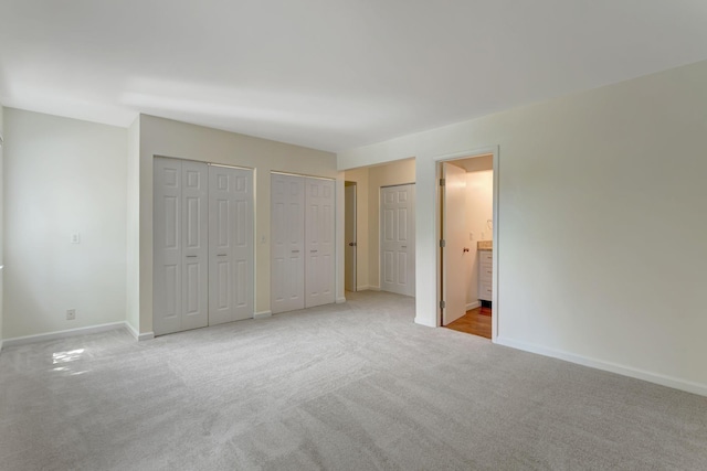 unfurnished bedroom with multiple closets, light carpet, and ensuite bath