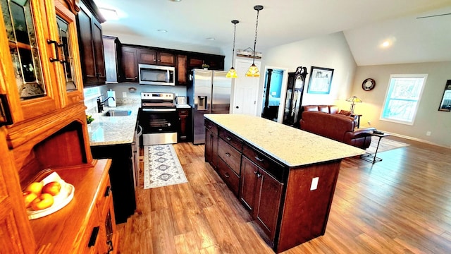 kitchen with vaulted ceiling, pendant lighting, a kitchen island, sink, and appliances with stainless steel finishes