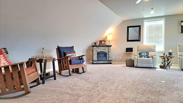 living area with ceiling fan, vaulted ceiling, a stone fireplace, and carpet flooring