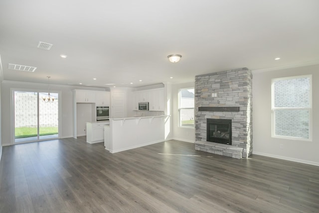 unfurnished living room with a chandelier, a stone fireplace, dark wood-type flooring, and crown molding