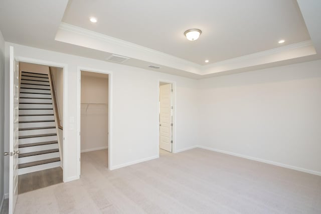 interior space with light carpet, a walk in closet, a raised ceiling, crown molding, and a closet