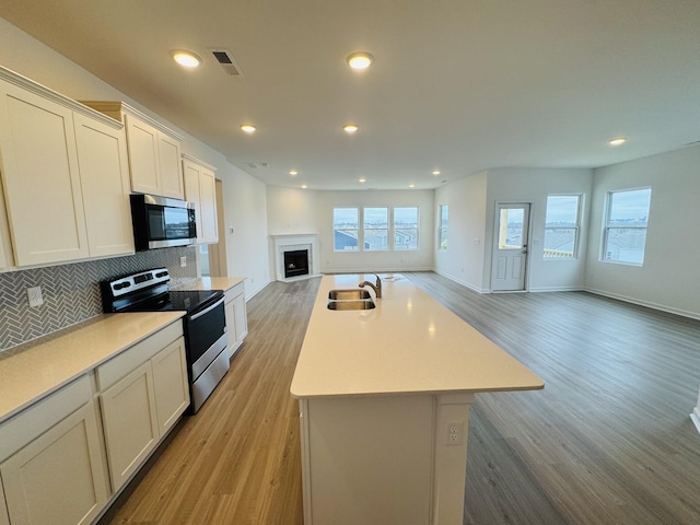 kitchen with sink, light hardwood / wood-style flooring, appliances with stainless steel finishes, a kitchen island with sink, and decorative backsplash