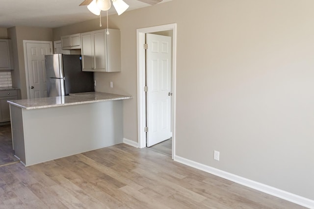 kitchen featuring kitchen peninsula, stainless steel fridge, light stone counters, ceiling fan, and light hardwood / wood-style floors