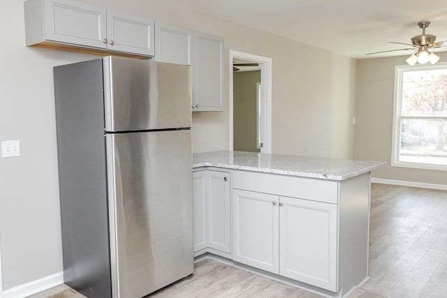 kitchen with white cabinets, ceiling fan, stainless steel fridge, light stone countertops, and light hardwood / wood-style floors