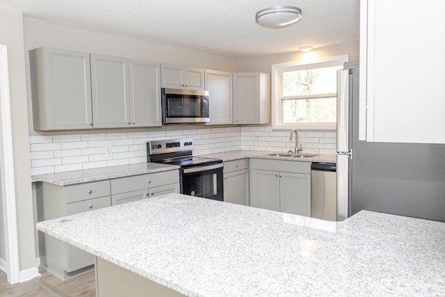 kitchen with appliances with stainless steel finishes, backsplash, gray cabinets, and sink