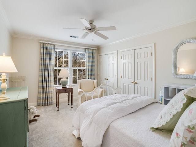 bedroom with ceiling fan, ornamental molding, light carpet, and two closets