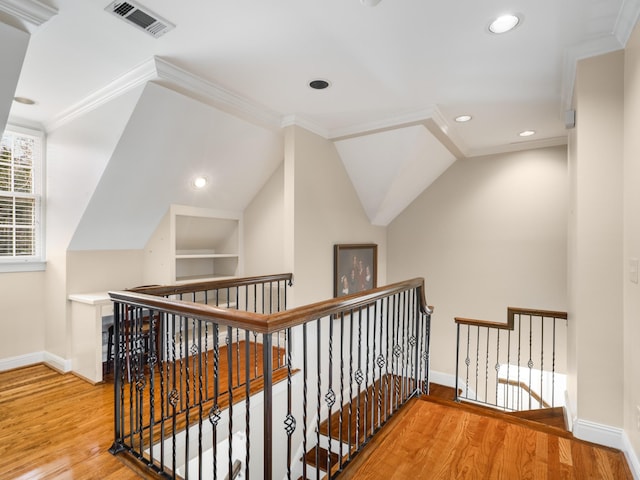 corridor with built in shelves, hardwood / wood-style flooring, vaulted ceiling, and ornamental molding