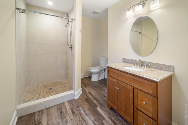 bathroom with hardwood / wood-style flooring, vanity, a tile shower, and toilet