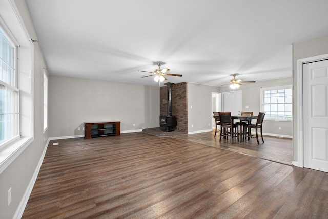 unfurnished living room with dark hardwood / wood-style floors, a wood stove, and ceiling fan