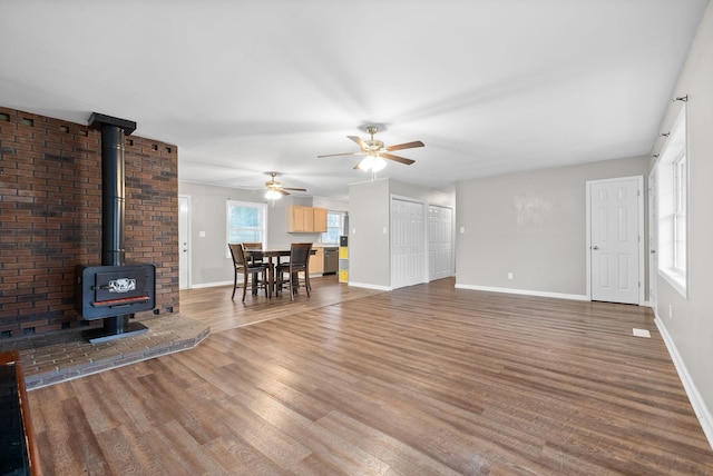 unfurnished living room with ceiling fan, wood-type flooring, and a wood stove