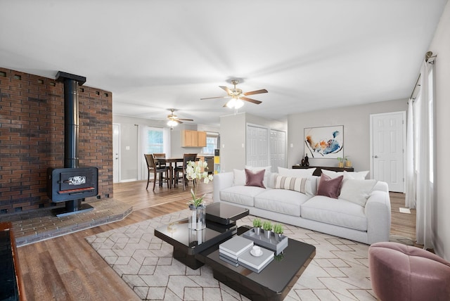 living room featuring light wood-type flooring, a wood stove, and ceiling fan