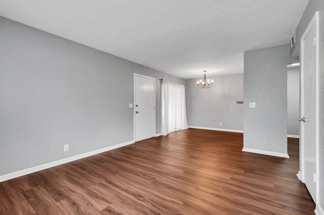 spare room featuring dark wood-type flooring and a chandelier