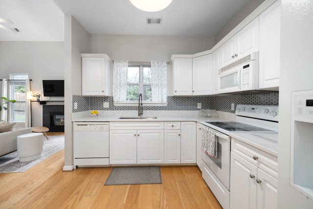 kitchen with light wood-type flooring, tasteful backsplash, white appliances, sink, and white cabinetry