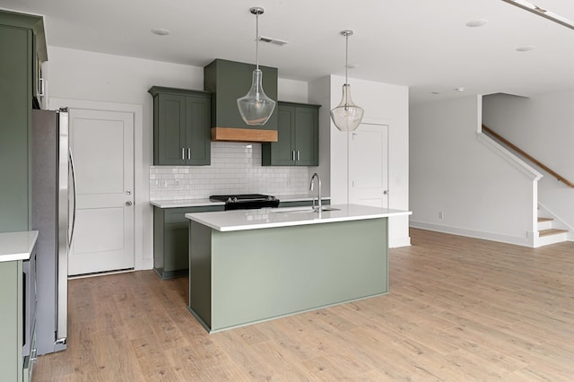 kitchen featuring sink, stainless steel fridge, a center island with sink, and tasteful backsplash