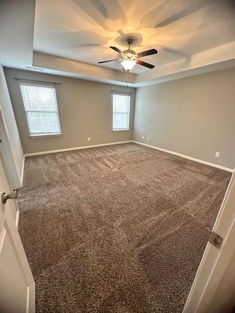 carpeted empty room featuring ceiling fan and a raised ceiling