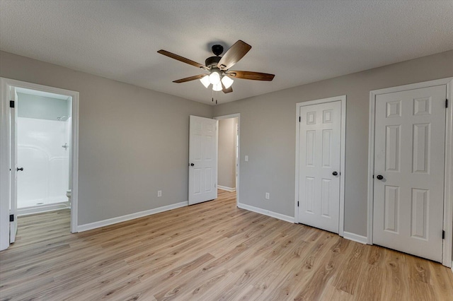 unfurnished bedroom featuring ensuite bath, a textured ceiling, two closets, ceiling fan, and light hardwood / wood-style floors