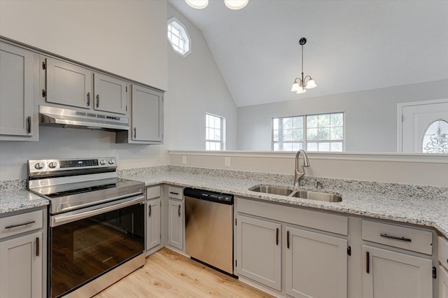 kitchen with light stone countertops, appliances with stainless steel finishes, light wood-type flooring, sink, and a notable chandelier