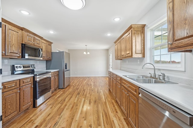 kitchen featuring pendant lighting, sink, light hardwood / wood-style flooring, appliances with stainless steel finishes, and a chandelier