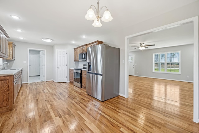 kitchen with ceiling fan with notable chandelier, stainless steel appliances, sink, light hardwood / wood-style floors, and hanging light fixtures