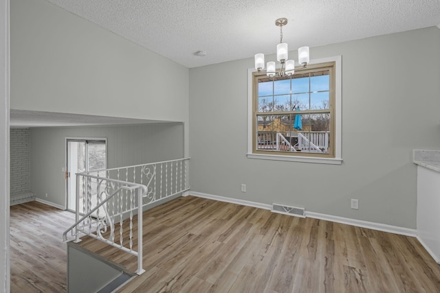 unfurnished room with an inviting chandelier, light hardwood / wood-style flooring, and a textured ceiling