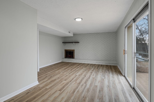 unfurnished living room with brick wall, a fireplace, light hardwood / wood-style flooring, and a textured ceiling