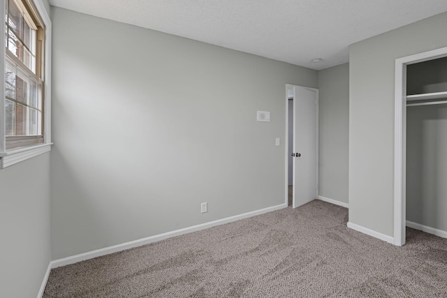 unfurnished bedroom featuring multiple windows, carpet floors, a closet, and a textured ceiling