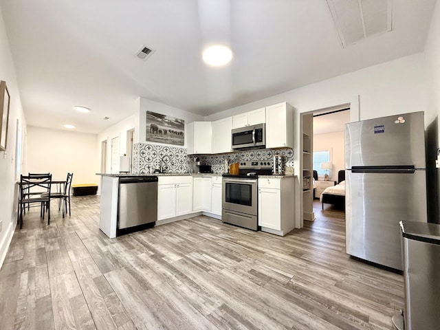 kitchen featuring light wood-type flooring, appliances with stainless steel finishes, decorative backsplash, and white cabinets