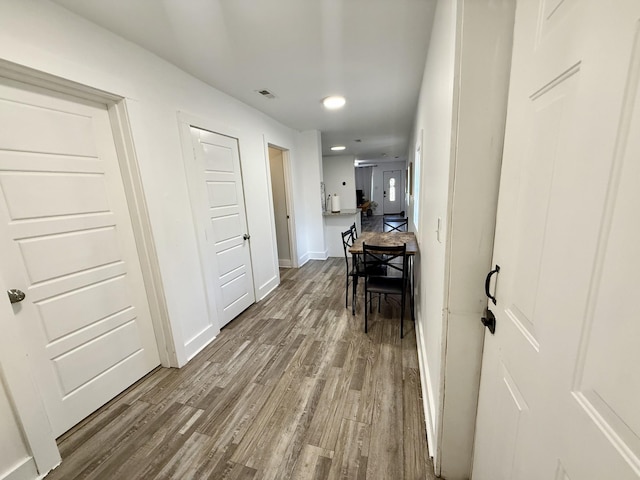 hallway with wood finished floors, visible vents, and baseboards