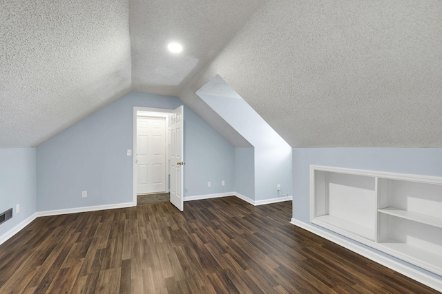 additional living space with built in shelves, a textured ceiling, vaulted ceiling, and dark wood-type flooring