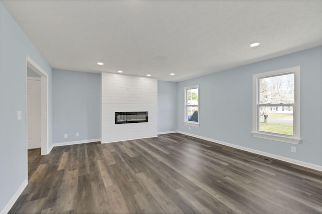 unfurnished living room with a textured ceiling, a large fireplace, and dark wood-type flooring