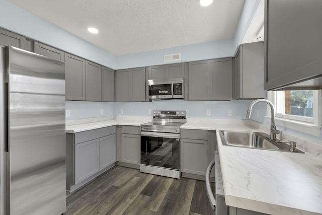 kitchen featuring gray cabinetry, sink, dark hardwood / wood-style floors, a textured ceiling, and stainless steel appliances