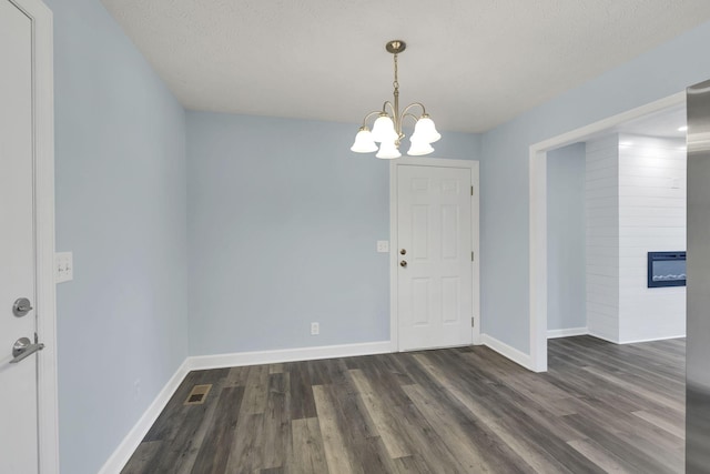 unfurnished room with a fireplace, dark hardwood / wood-style flooring, a chandelier, and a textured ceiling