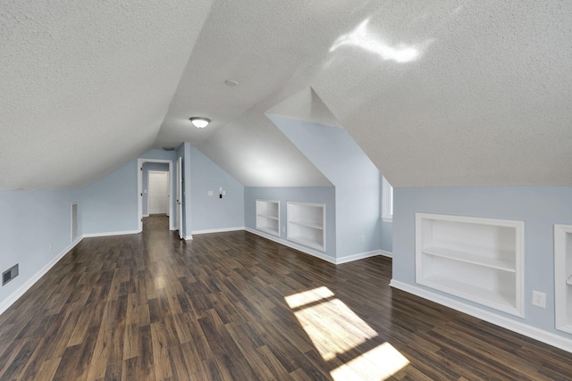 additional living space with built in shelves, dark hardwood / wood-style floors, lofted ceiling, and a textured ceiling