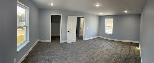 unfurnished bedroom with multiple windows, dark carpet, and a spacious closet