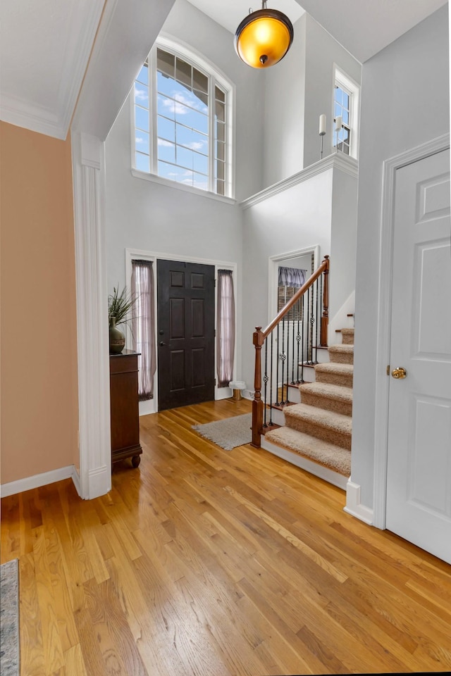 foyer entrance featuring a towering ceiling, light hardwood / wood-style flooring, and ornamental molding