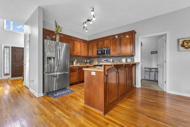 kitchen with a kitchen breakfast bar, light wood-type flooring, tasteful backsplash, kitchen peninsula, and stainless steel appliances