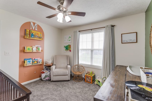 carpeted bedroom with a nursery area, a textured ceiling, and ceiling fan