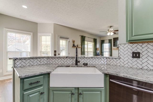 kitchen featuring sink, green cabinets, light stone countertops, stainless steel dishwasher, and kitchen peninsula