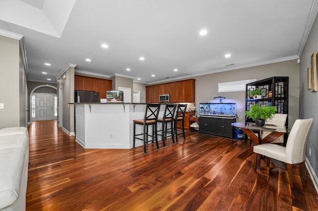 kitchen featuring kitchen peninsula, a kitchen breakfast bar, dark hardwood / wood-style flooring, ornamental molding, and fridge