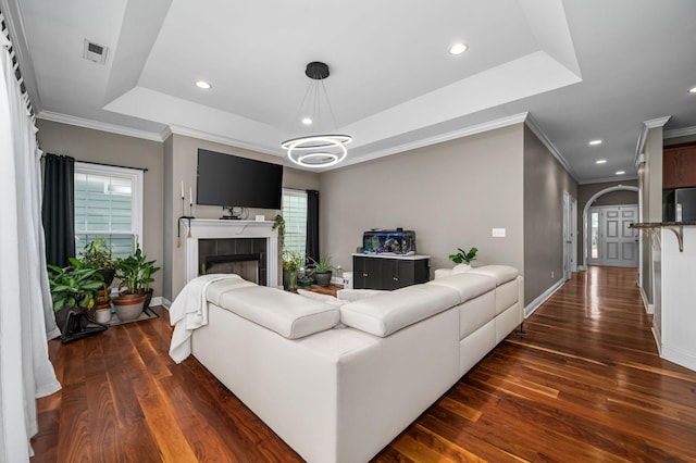 living room featuring plenty of natural light, dark hardwood / wood-style flooring, a tiled fireplace, and a tray ceiling